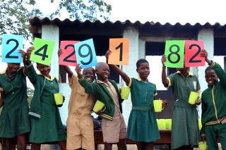 I bambini tengono in alto dei cartelli per celebrare la nuova cifra di alimentazione di Mary's Meals.